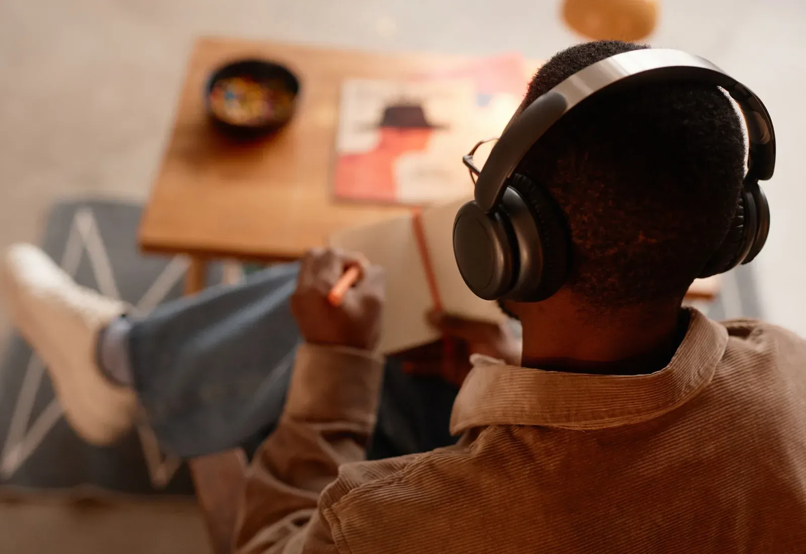 Person seen from behind, wearing headphones, drawing in a notebook.