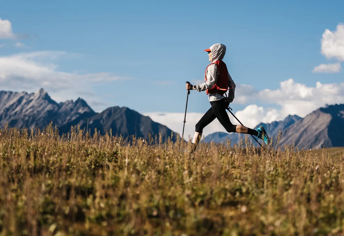 Randonneuse qui court dans une prairie, face aux montagnes.