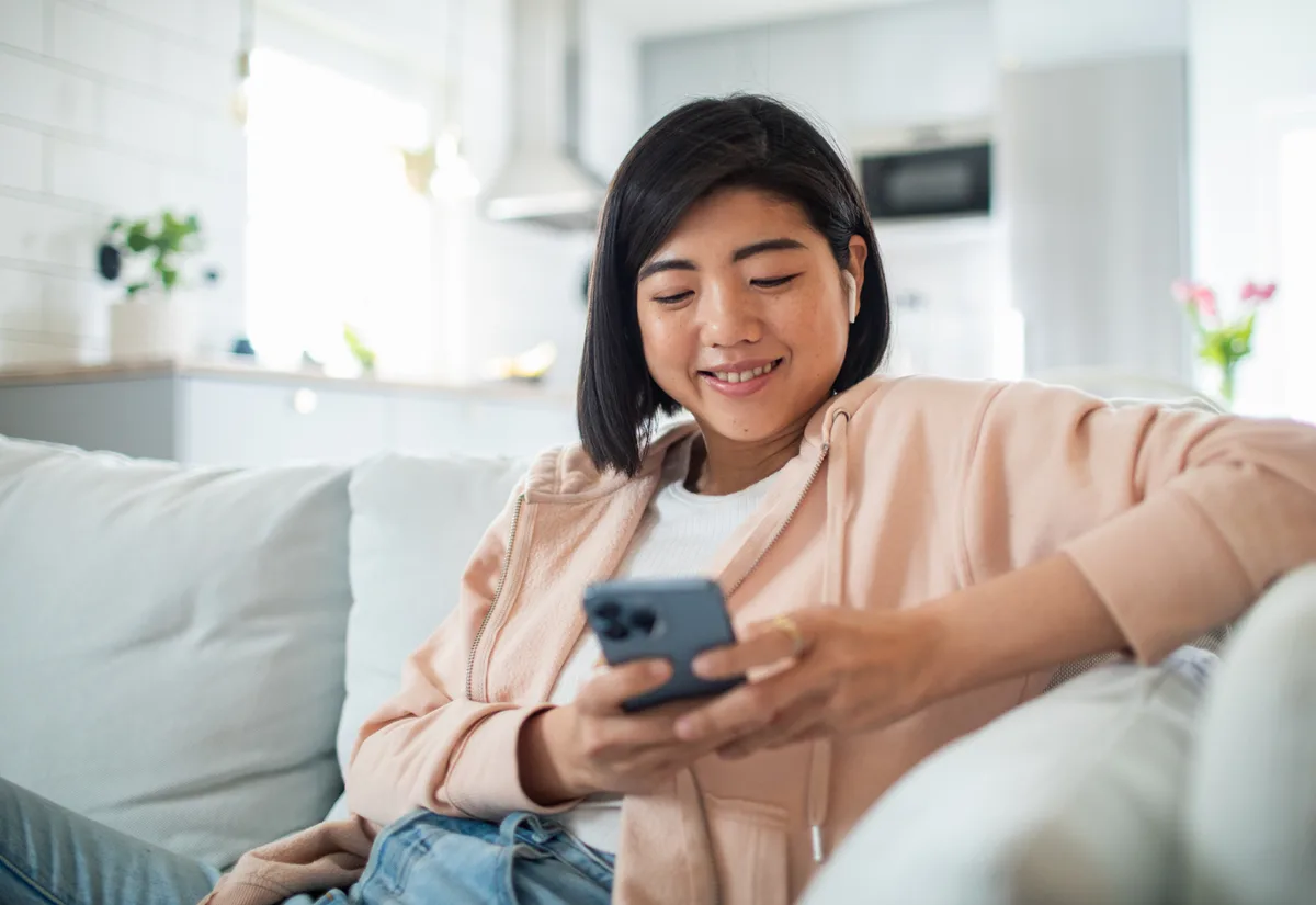 Femme souriante sur un canapé, qui consulte son téléphone.